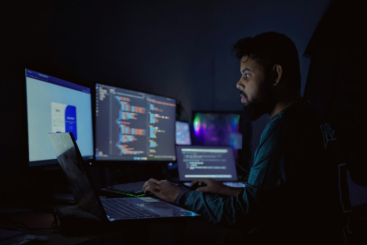 A developer working across three monitors in a dark room